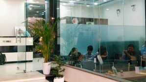 Un bureau avec des cloisons en verre, un comptoir d’accueil et un escalier.