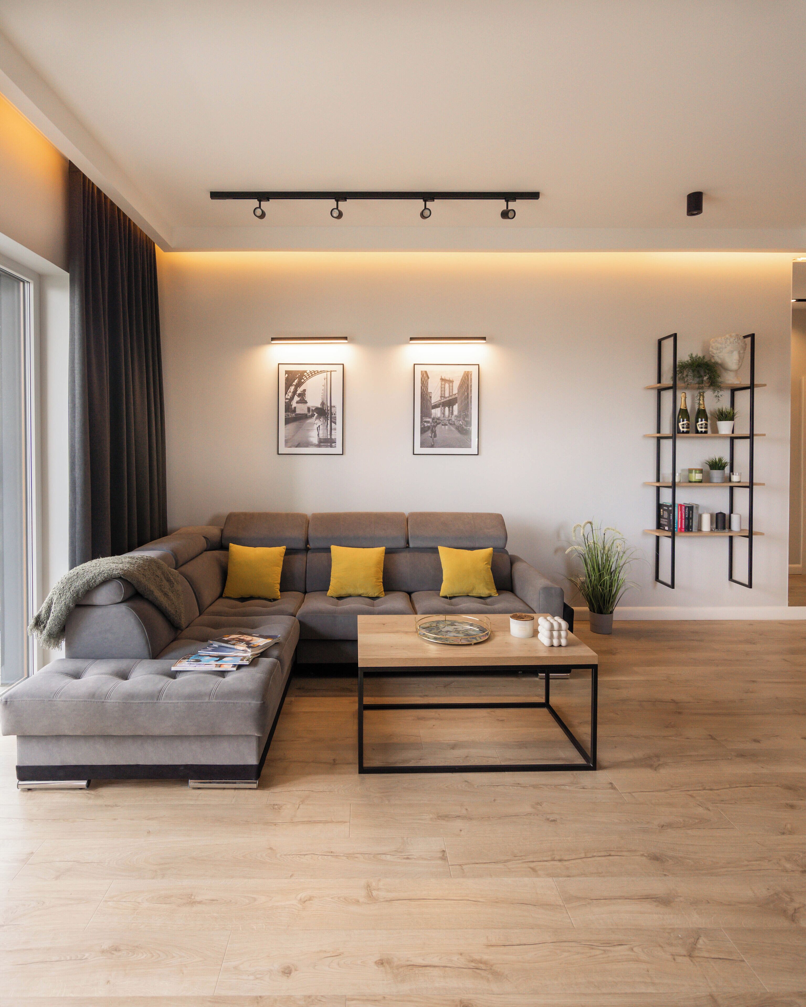 A modern living room with a grey sectional sofa, a wooden coffee table, and a bookshelf with books and decorative items.