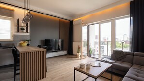 Ein modernes Wohnzimmer mit Couch, Fernseher, Holztisch und einem großen Fenster mit Blick auf die Stadt.