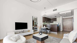 Una sala de estar moderna con un televisor de pantalla plana, un sofá blanco, un sillón tipo bean bag y una mesa de centro con un jarrón de flores.