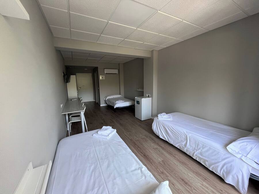 Habitación de hotel con dos camas individuales, un escritorio, una silla, un refrigerador pequeño y un aire acondicionado.