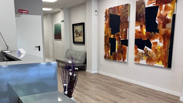 A reception area with a blue counter, a framed picture on the wall, and two abstract paintings. - Unicorn Residence for Students (Valencia)