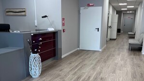 A reception area with a desk, a white vase with dried flowers, a fire alarm, and a door in the background. - Unicorn Residence for Students (Valencia)