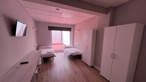 A hotel room with two single beds, a desk with a chair, a wardrobe, and a TV on the wall. - Unicorn Residence for Students (Valencia)