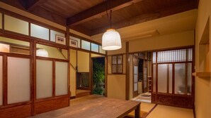 Una habitación japonesa tradicional con suelo de tatami, una mesa de madera, puertas correderas y una lámpara colgante.