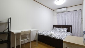 A small, well-lit room with a single bed, a desk, and a chair.