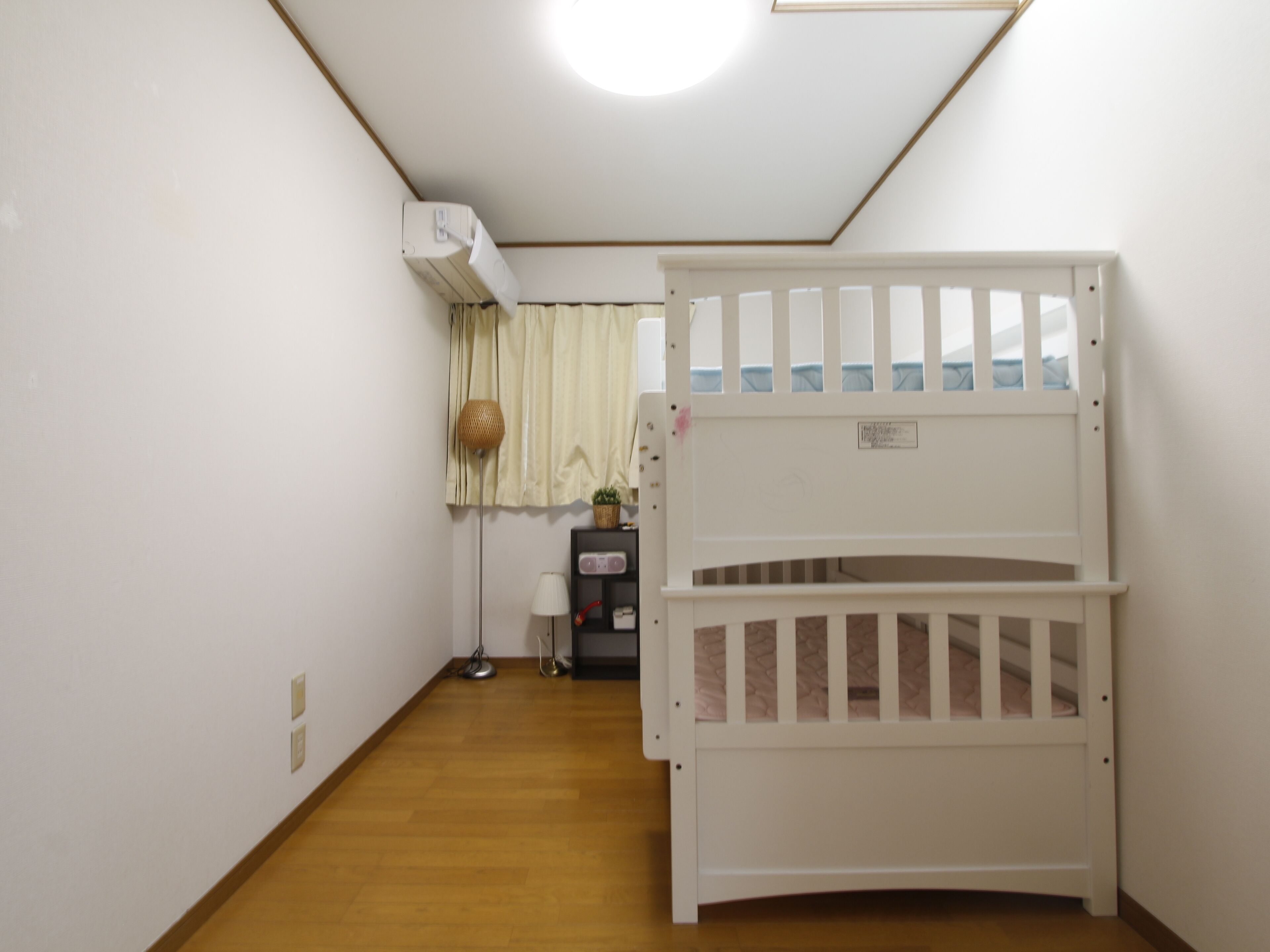 Een kamer met een stapelbed, een klein bureau met stoel, een lamp en een raam met gordijnen.