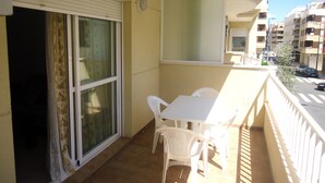 En balkon med bord og stole, en skydedør i glas samt udsigt til gaden og bygningerne.
