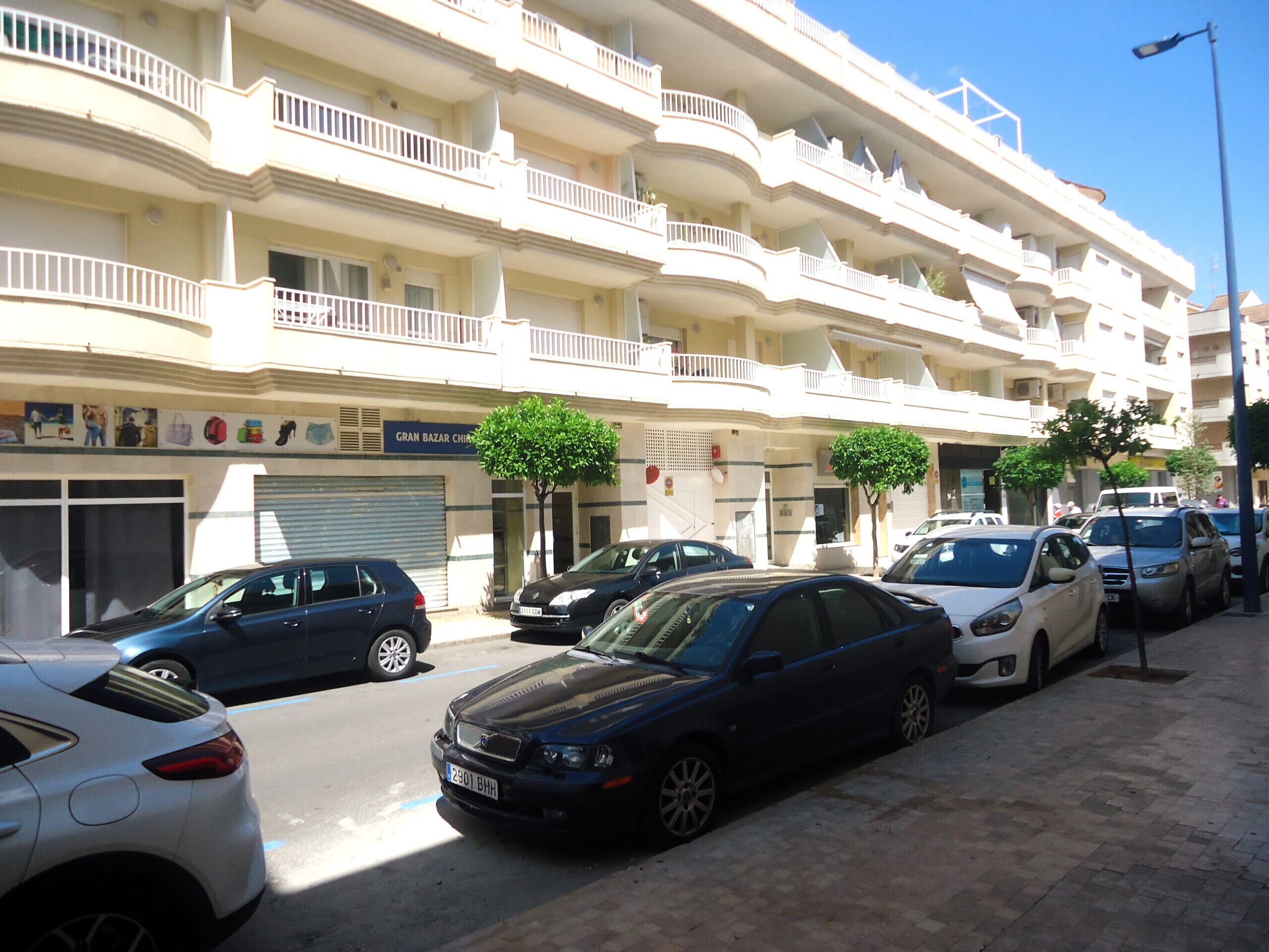 A multi-story building with balconies, parked cars, and a sign for 'GRAN BAZAR CHIM'.