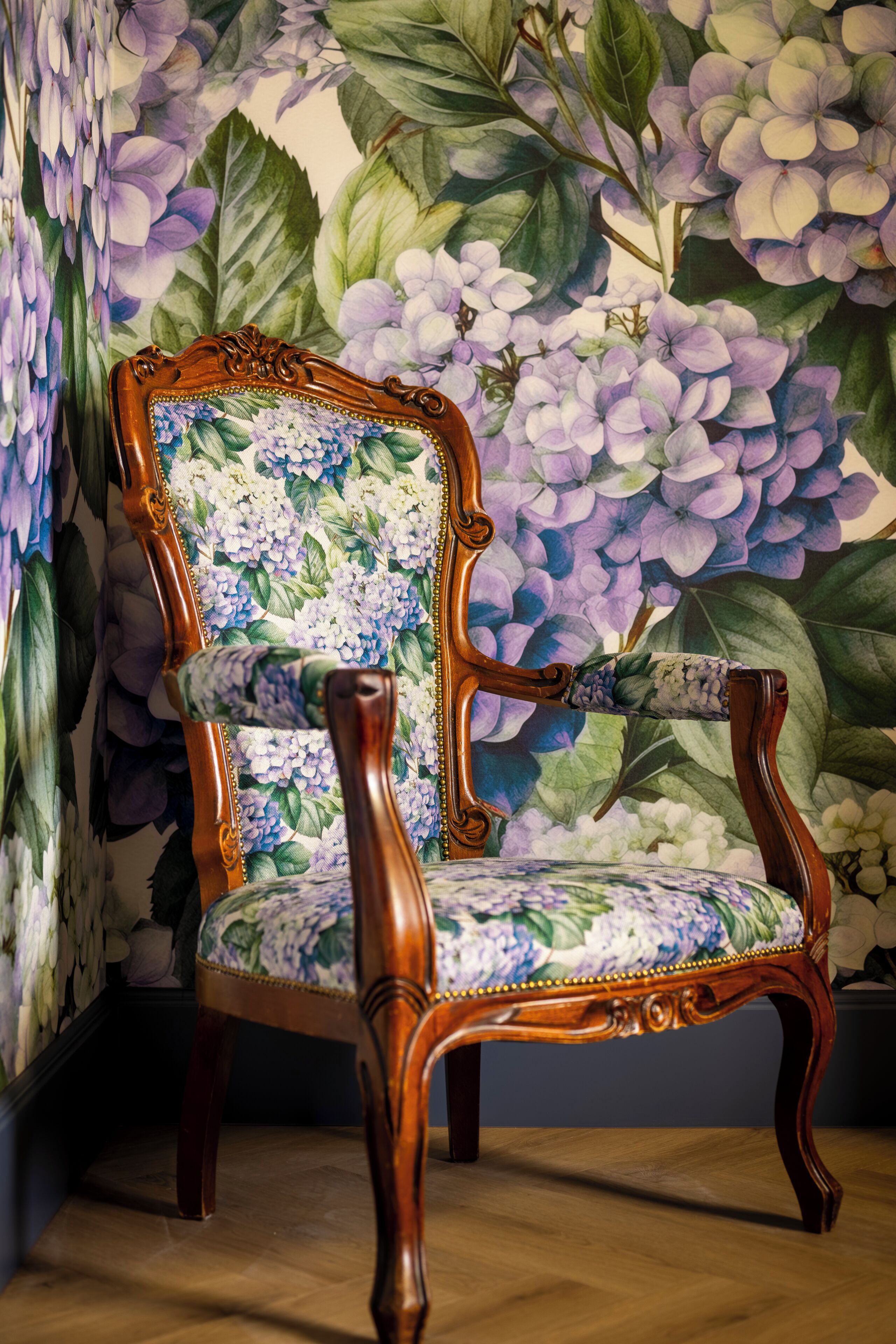 Une chaise en bois dotée d’un siège et d’un dossier rembourrés avec un motif floral, placée devant un mur recouvert d’un grand papier peint à motifs floraux.