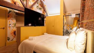 Quarto com cama, televisão, chuveiro e parede de tijolos.