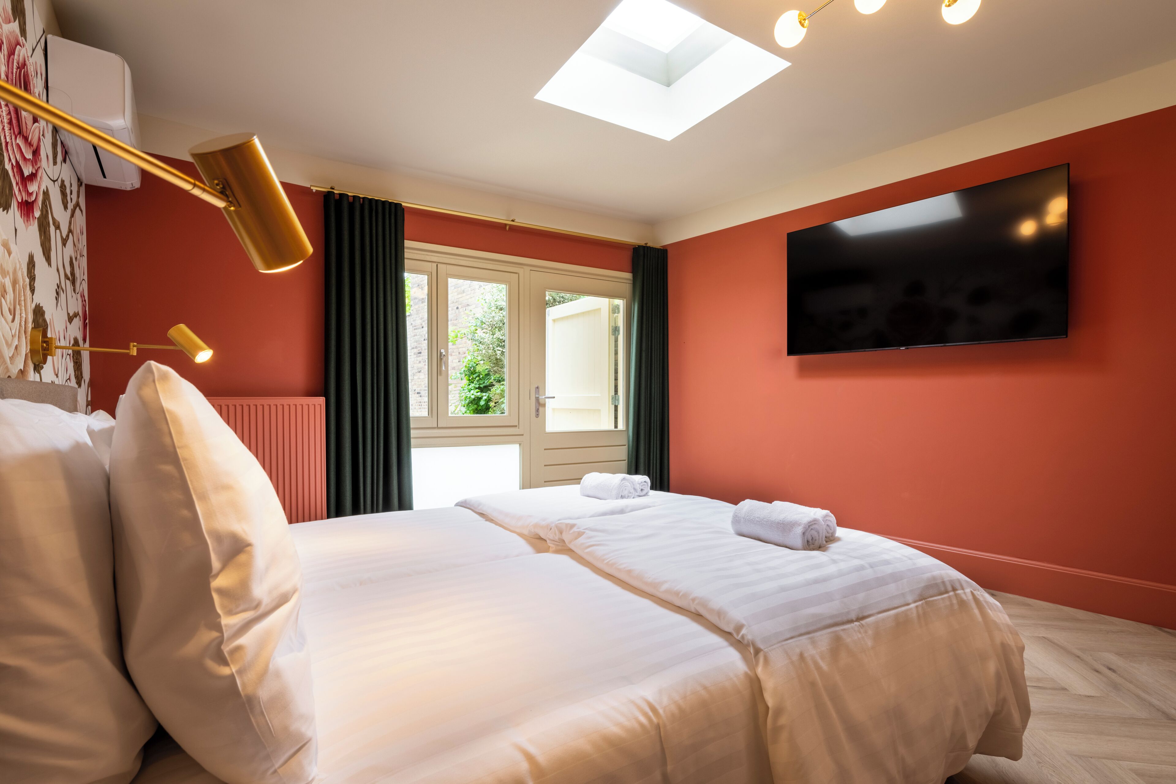 Une chambre d’hôtel avec un grand lit, un téléviseur à écran plat fixé au mur, une fenêtre de toit et une fenêtre avec des rideaux.