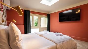 Une chambre d’hôtel avec un grand lit, un téléviseur à écran plat fixé au mur, une fenêtre de toit et une fenêtre avec des rideaux.