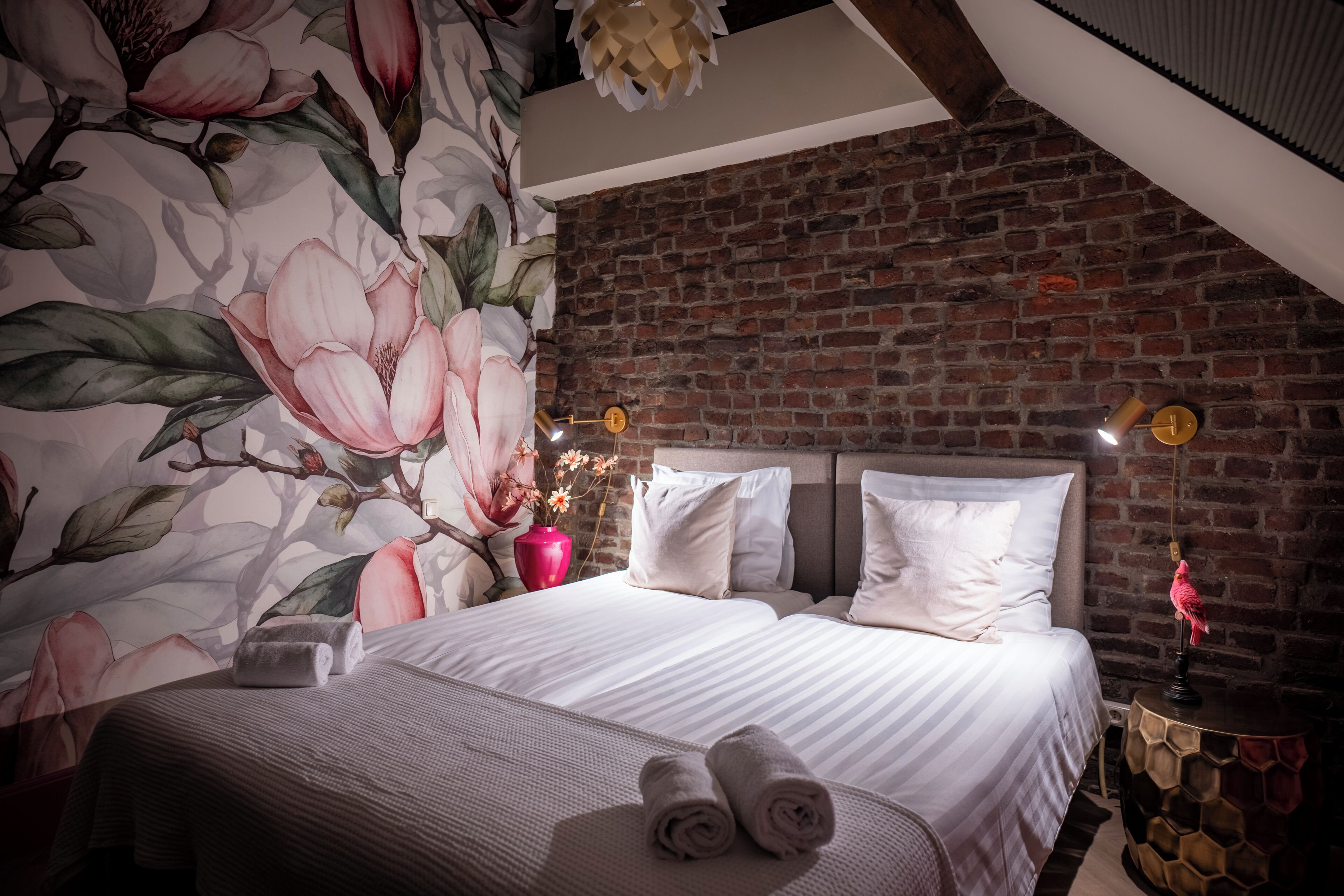 Habitación de hotel con una cama grande, una pared de ladrillo y un mural floral.