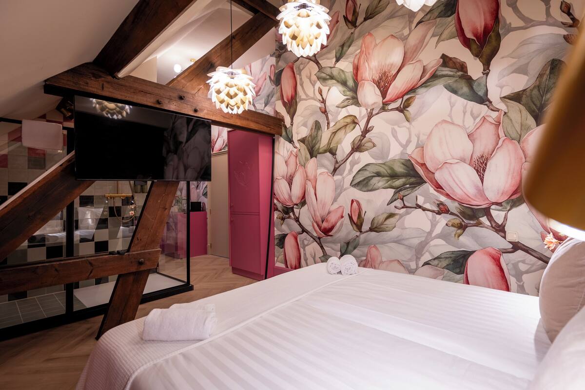 Un dormitorio con una cama grande, techo de madera, armario rosa y papel tapiz floral.