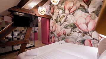A bedroom with a large bed, a wooden ceiling, a pink wardrobe, and a floral wallpaper.