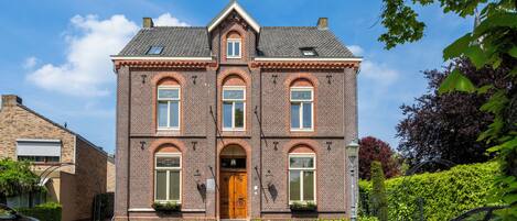A two-story brick building with a central entrance, large windows, and a sloped roof.