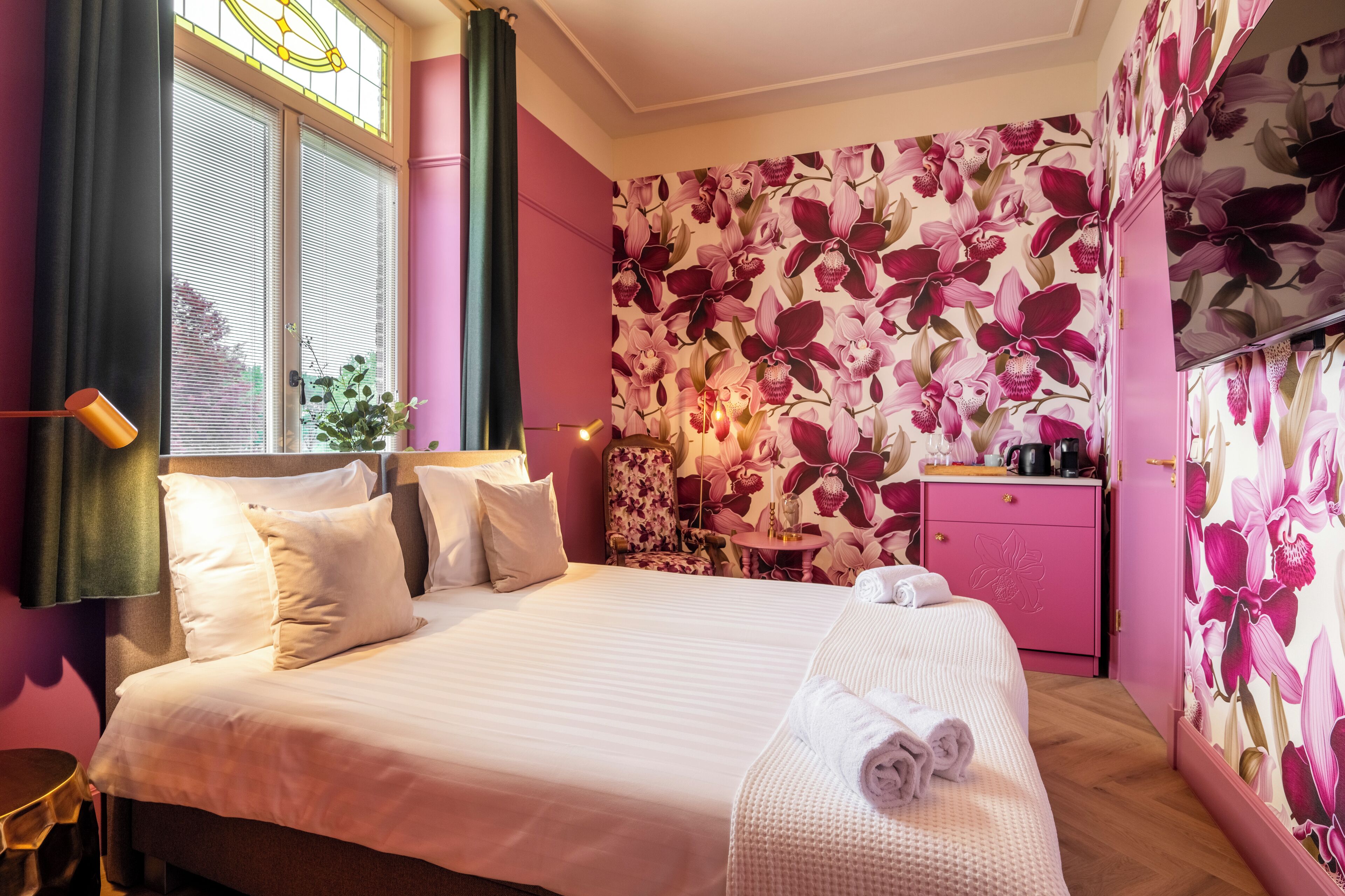 Een hotelkamer met een bed, een bureau, een stoel, een bijzettafeltje en een plant in een pot.
