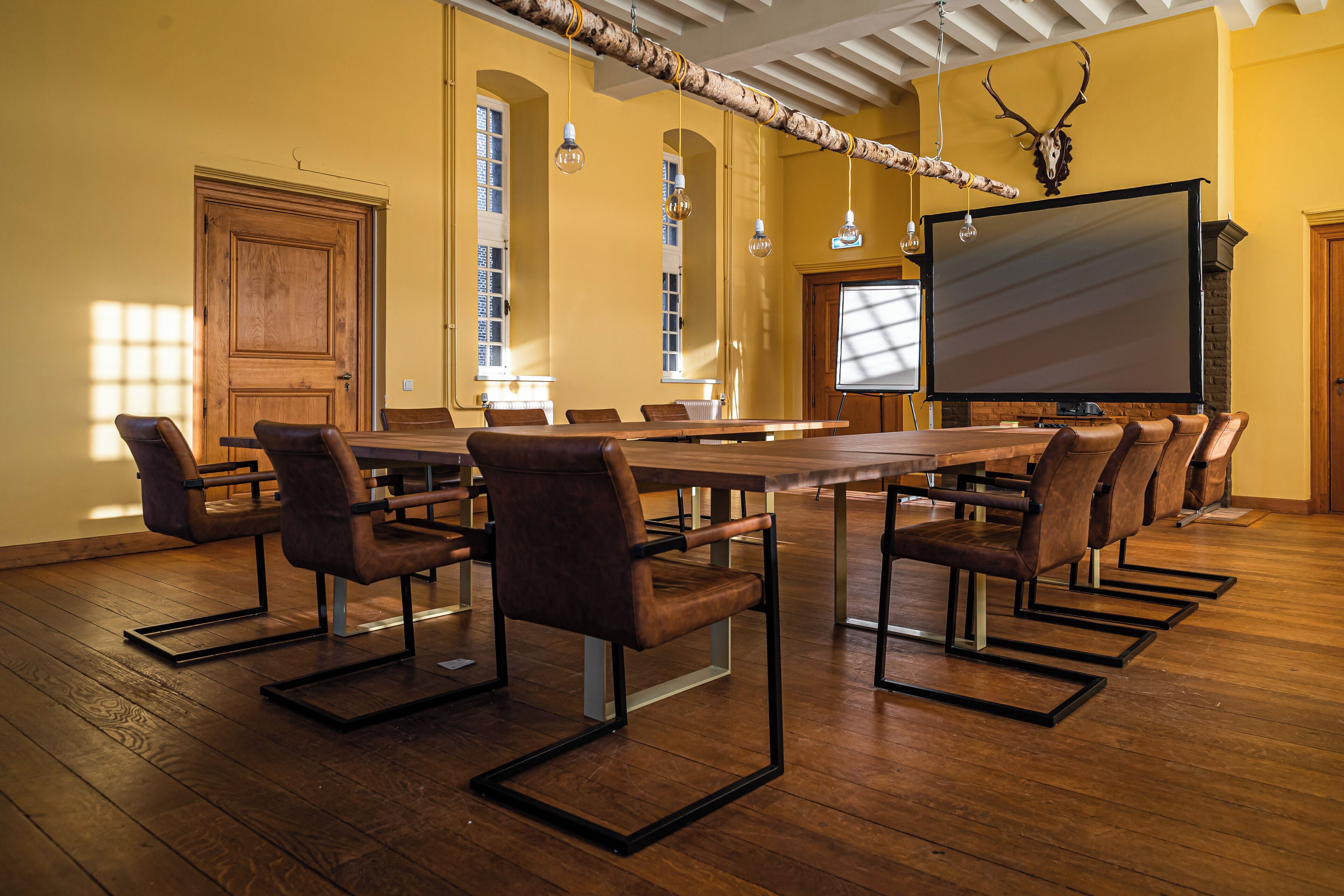 A conference room with a long table, multiple chairs, a large screen, and a wooden ceiling.
