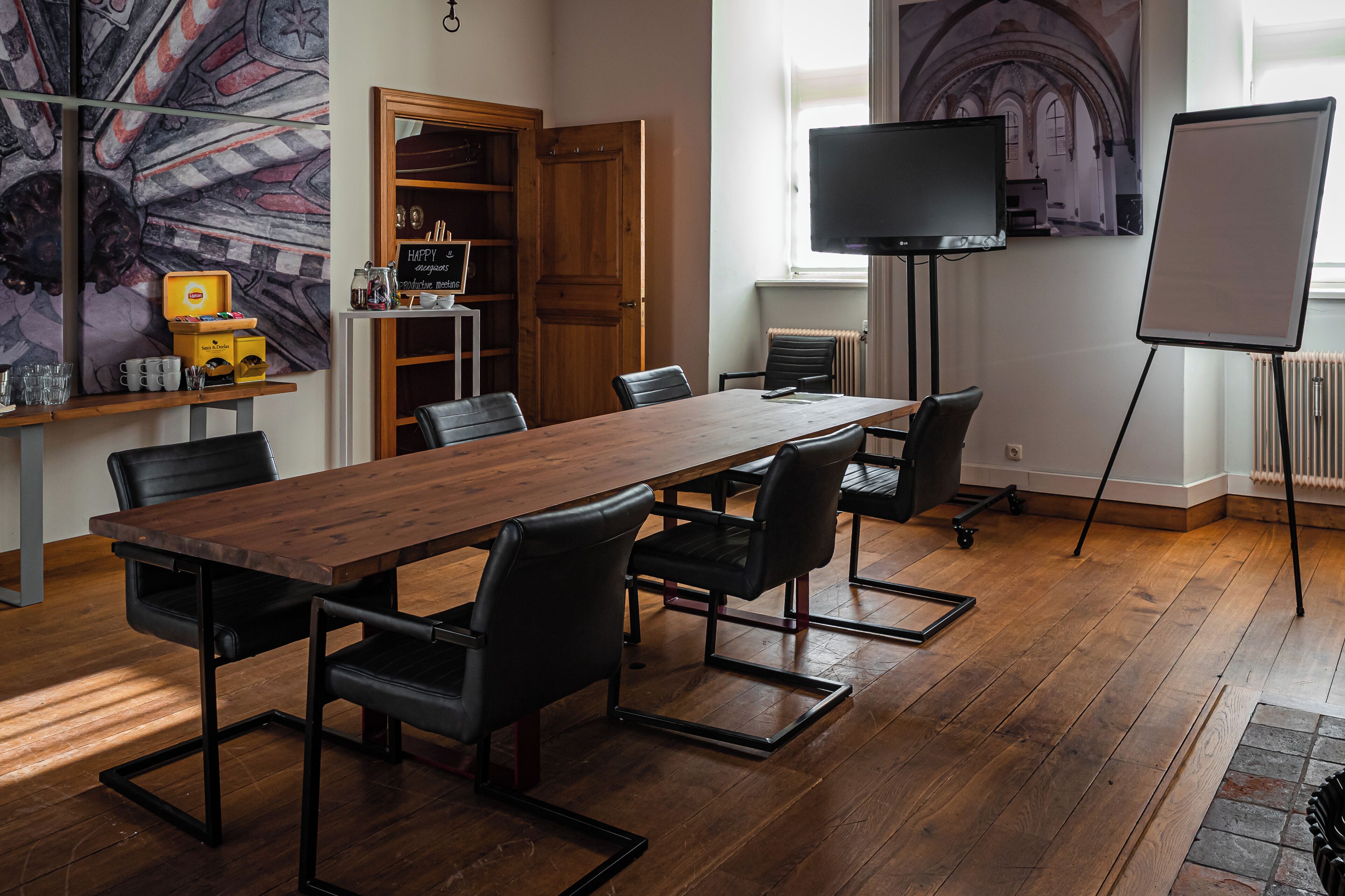 A conference room with a long wooden table, black chairs, a television, and a whiteboard.