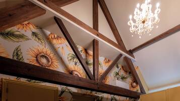 Quarto com vigas de madeira aparentes, papel de parede com padrão floral e um lustre.