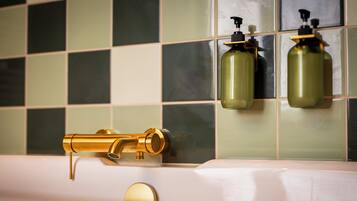 Une salle de bain avec un robinet doré, deux distributeurs de savon et un mur recouvert de carreaux.