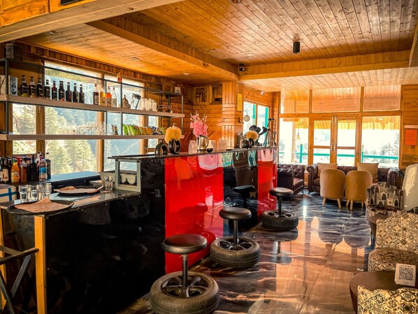 Zona de bar con interior de madera, taburetes y varios botellones en estanterías.