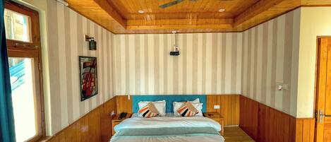 A bedroom with a wooden ceiling, a bed with a blue headboard, striped wallpaper, and a ceiling fan.