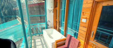 A wooden cabin with a glass balcony, a white bathtub, and a red chair.
