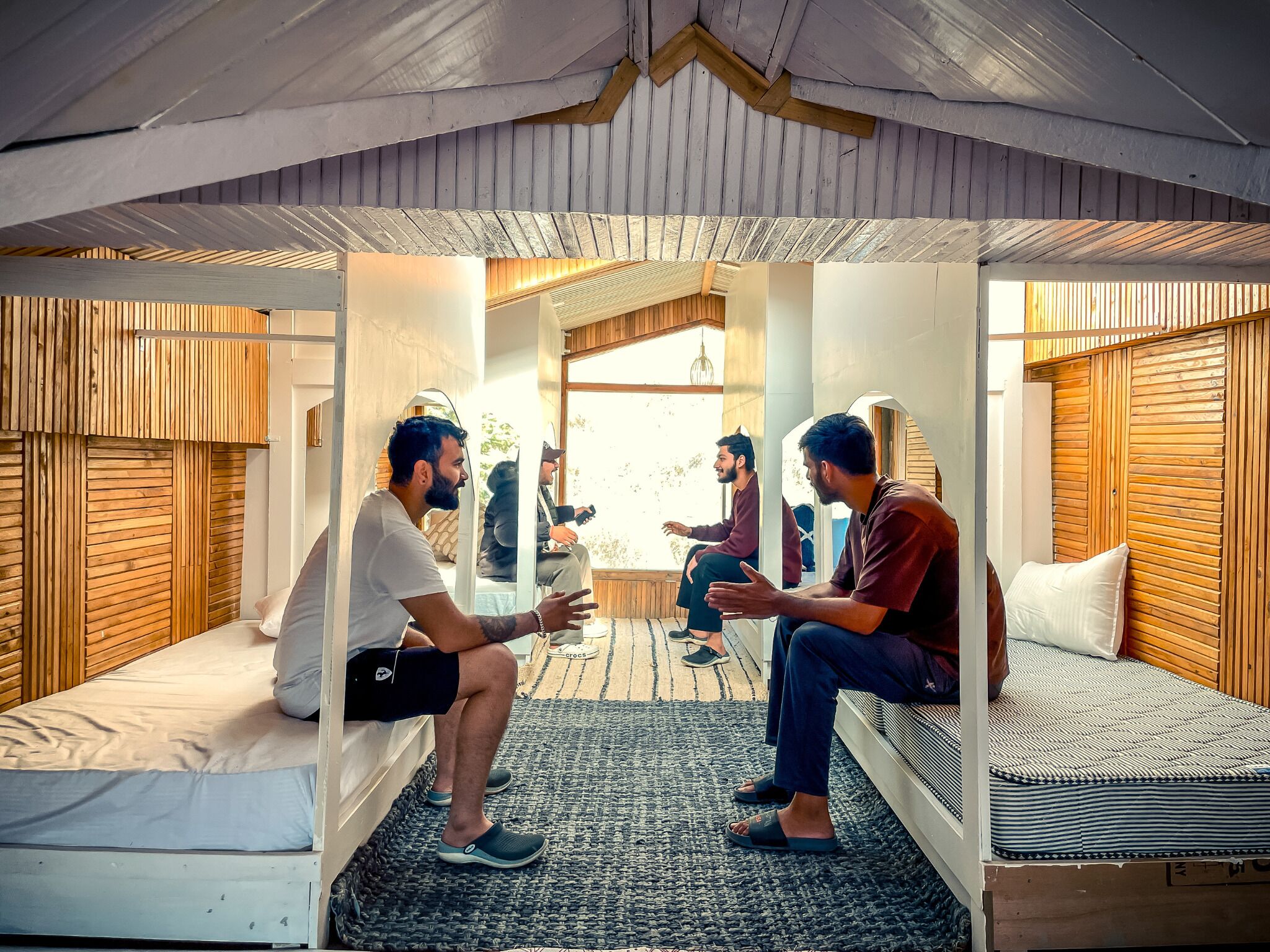 A cozy room with wooden paneling, a large window, and a bed with a patterned mattress.