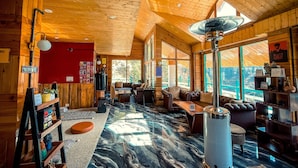 A cozy cabin interior with wooden walls and ceiling, a marble floor, a fireplace, and a large window offering a scenic view. - The Elevia Hotels (Banjar)