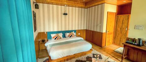 A bedroom with a bed, a wooden ceiling fan, a nightstand, a bedside table with a vase of flowers, and a door leading to a bathroom.