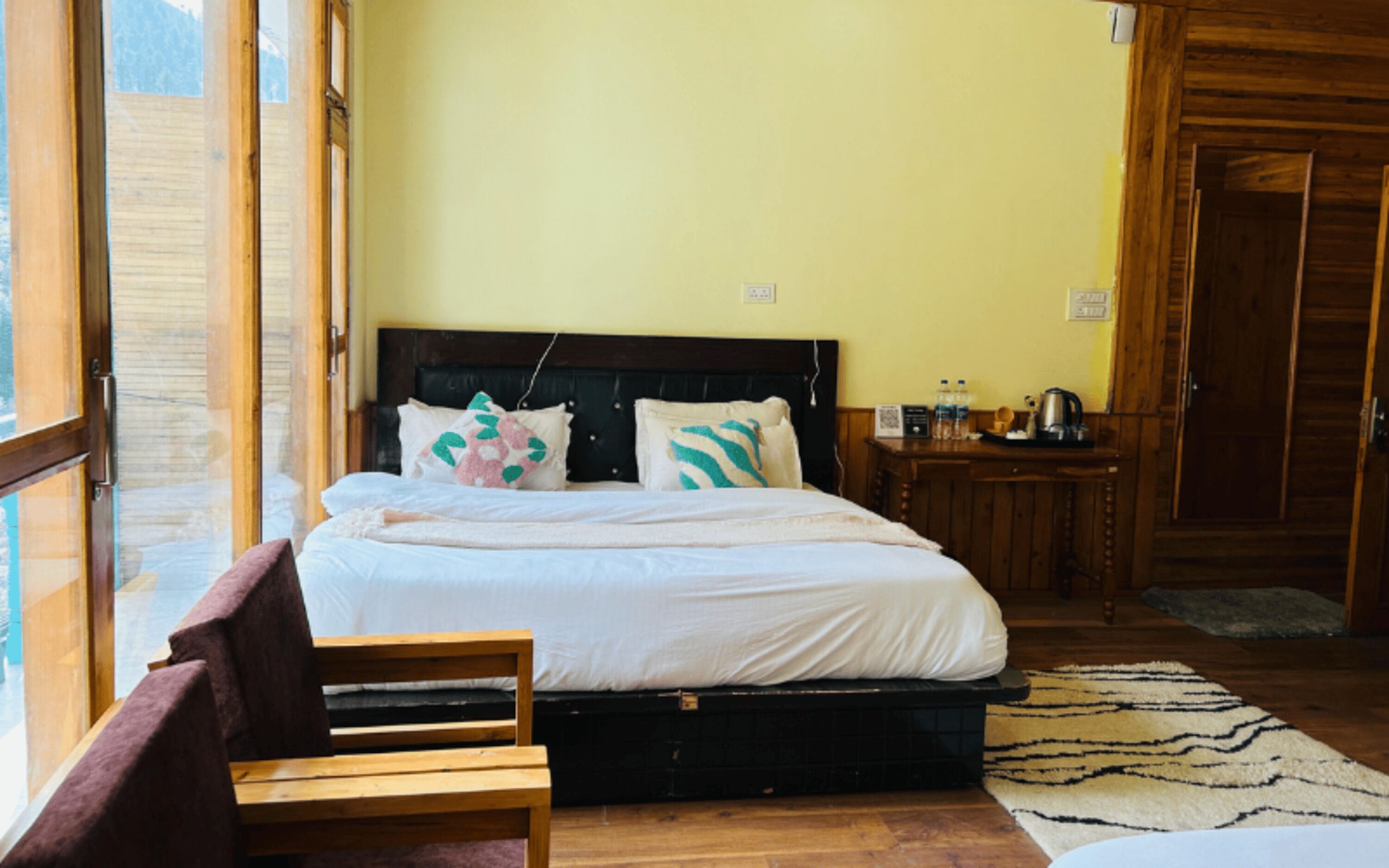 Une chambre à coucher avec un lit, une tête de lit en bois, un banc, un tapis et une petite table sur laquelle sont posés divers objets.