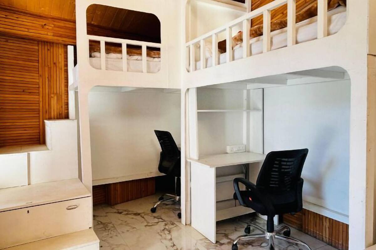 Quarto com beliche, escrivaninha e cadeira, um pequeno armário e janela com persianas de madeira.