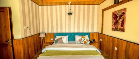 Un dormitorio con cabecera de madera, cama con ropa blanca, mesita de noche con lámpara e iluminación empotrada en la pared.