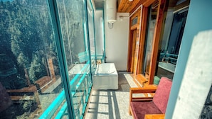 A balcony with a glass wall, a wooden chair, a small table, and a white bathtub. - The Elevia Hotels (Banjar)