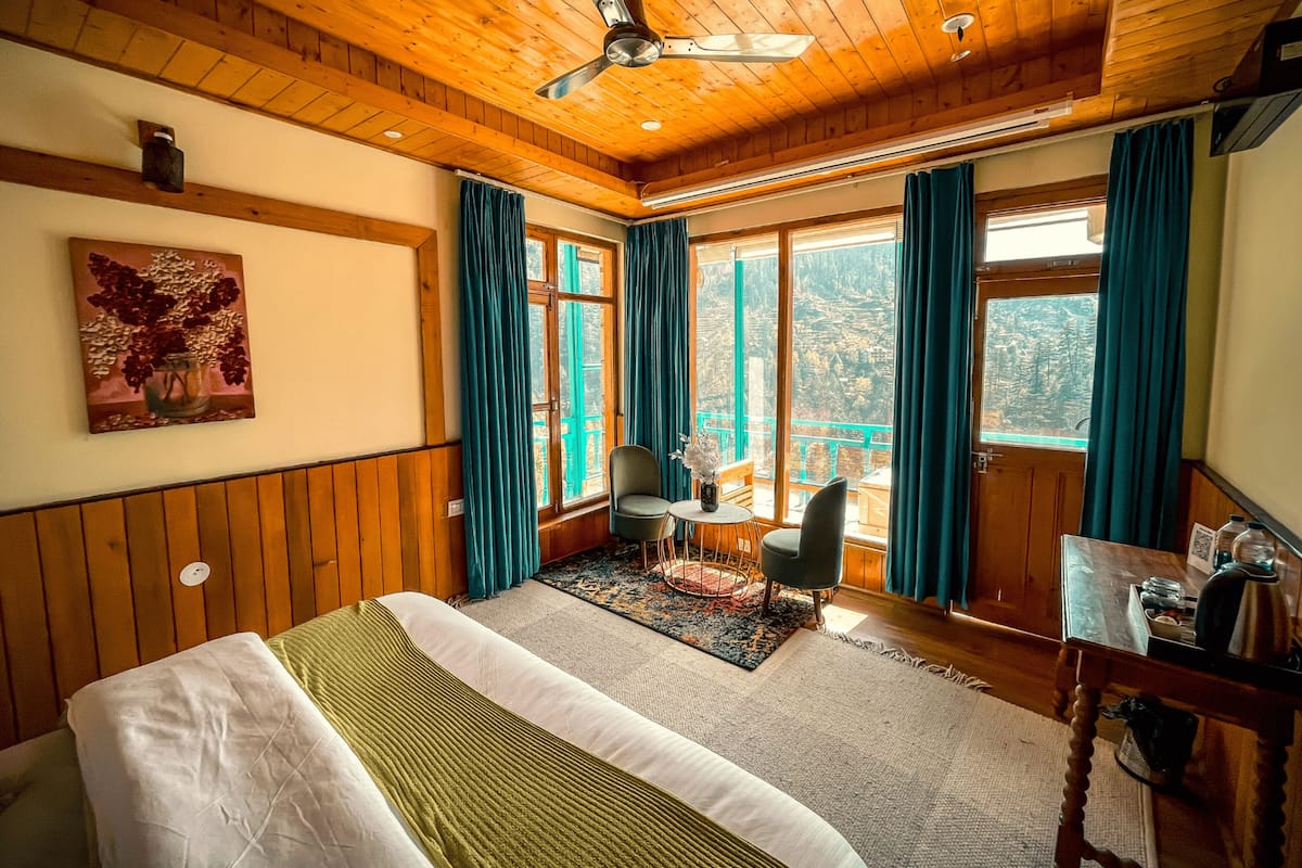 Quarto com cama, mesa e cadeira. Tem cortinas nas janelas e um ventilador de teto.