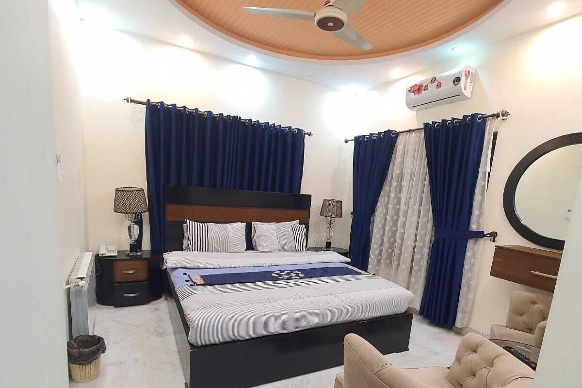 A bedroom with a bed, a chair, a ceiling fan, and a small table with a lamp.