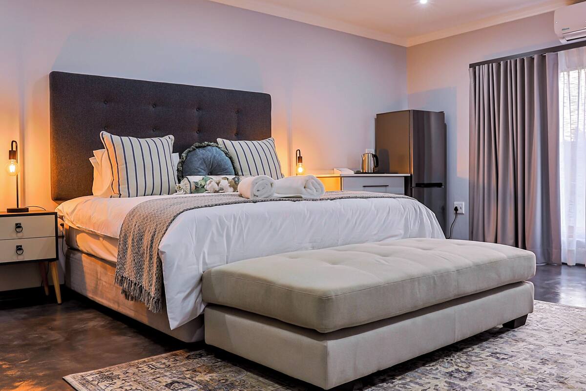 Une chambre moderne avec un grand lit, des tables de chevet, une armoire et une vue sur l’extérieur.