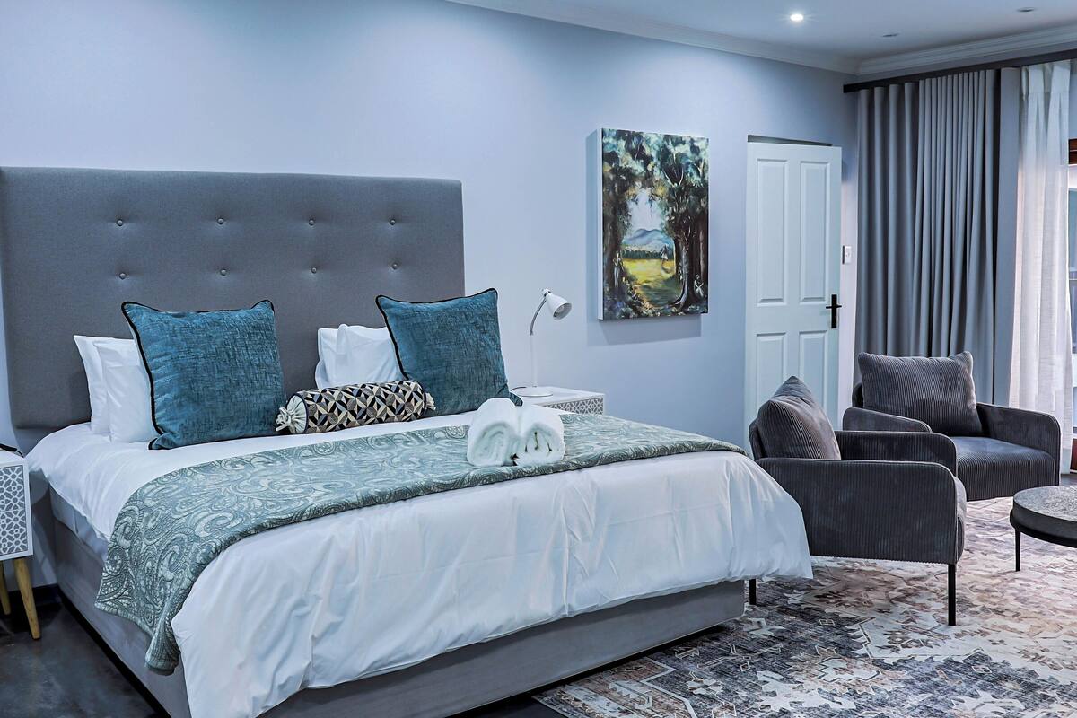 Une chambre à coucher moderne avec un grand lit, une tête de lit rembourrée de couleur grise et un tableau accroché au mur.
