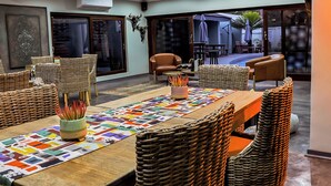 Een eetruimte met rieten meubels, een houten tafel en een kleurrijke tafelkleed.