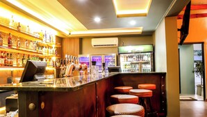 Een bar met krukken, een toonbank met kassa en planken vol flessen.
