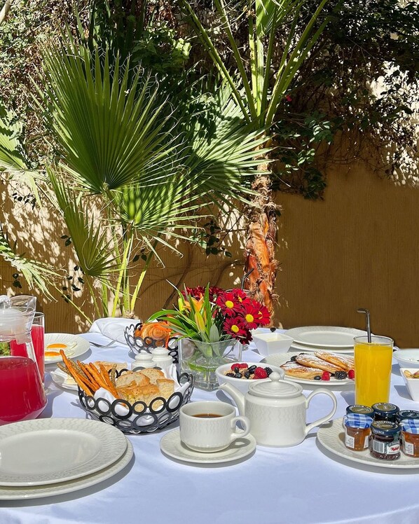 Taula de petit esmorzar a l'aire lliure plena d'una varietat d'aliments, com ara pastissos, fruita i begudes.