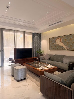 A modern living room with a flat-screen TV, a coffee table, a sofa, and a large abstract painting on the wall. - Vivienda Hotel Villas Al Hada (Riyadh)
