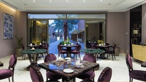 A dining area with multiple tables and chairs, a large window with a view of palm trees, and a modern interior design.