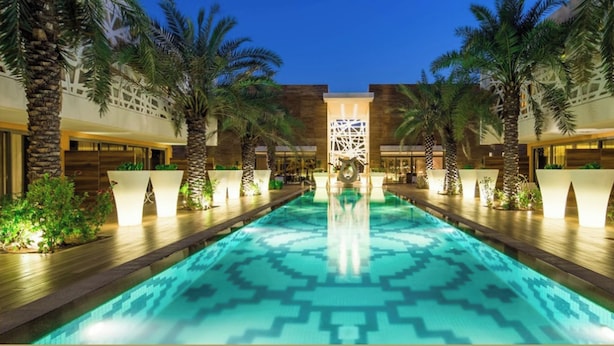 A pool area with a geometric tile pattern, surrounded by palm trees and modern architecture.
