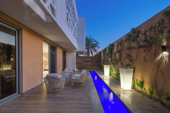 A modern outdoor patio with wicker furniture, a blue-lit water feature, and a view of the building's exterior.
