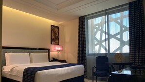 A hotel room with a bed, a desk, a chair, a lamp, and a window with curtains.