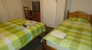 Two single beds with green checkered bedding, a wooden chair, a small table, and a white wardrobe.