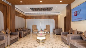 A spacious lobby with plush seating, a marble floor, and a large screen displaying the hotel name.